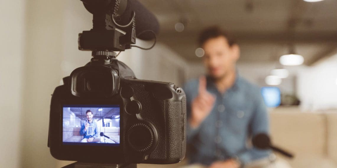 Male vlogger recording content for his video blog. Young man in focus on digital camera screen.