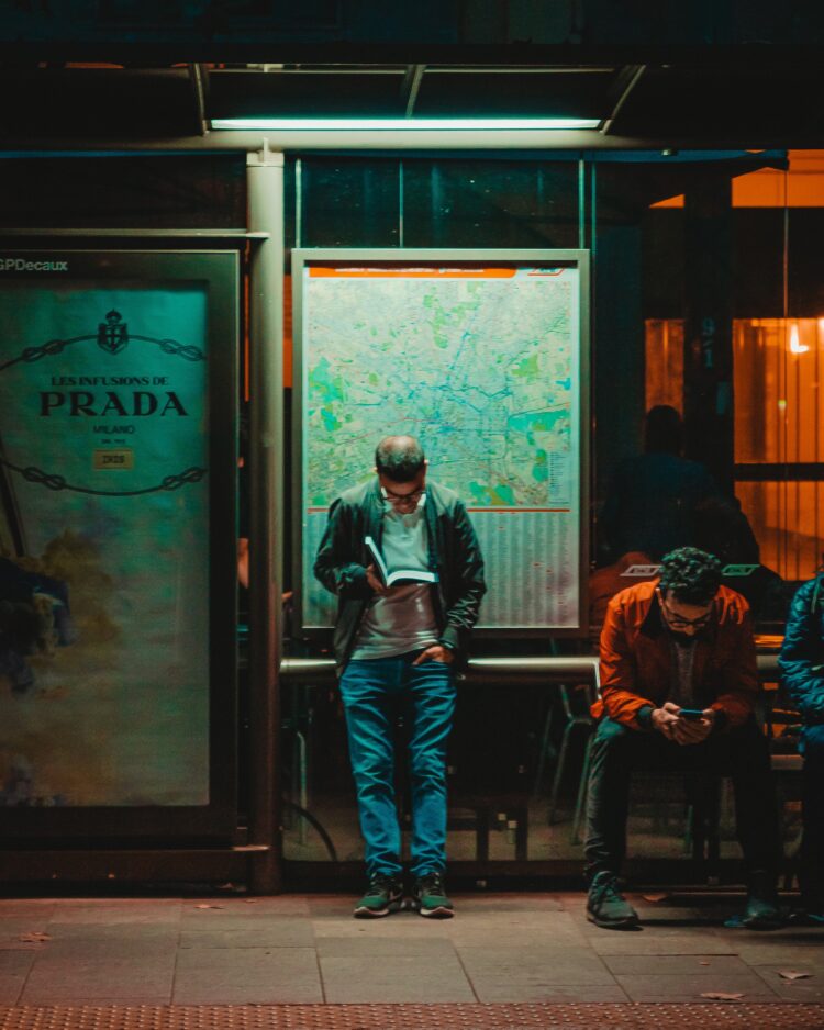 standing man reading book beside sitting man using phone