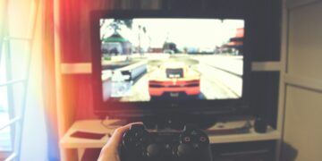 person holding Sony PS3 controller in front of flat screen monitor