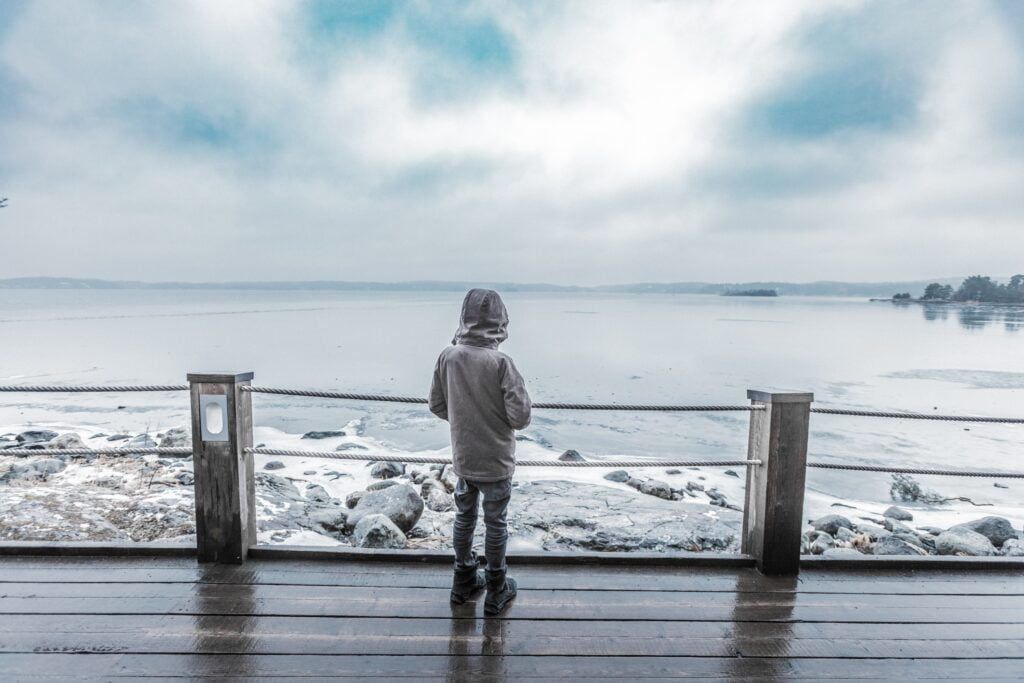 Kind steht vor der Küste auf brauner Plattform