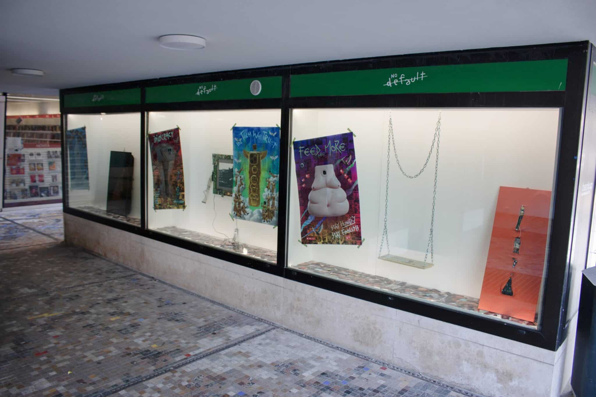 L'installazione Atrophia nelle tre vetrine di Piazzale Candiani a Mestre: poster, un'altalena con tastiera al posto del seggiolino e un pannello arancione con schede elettroniche