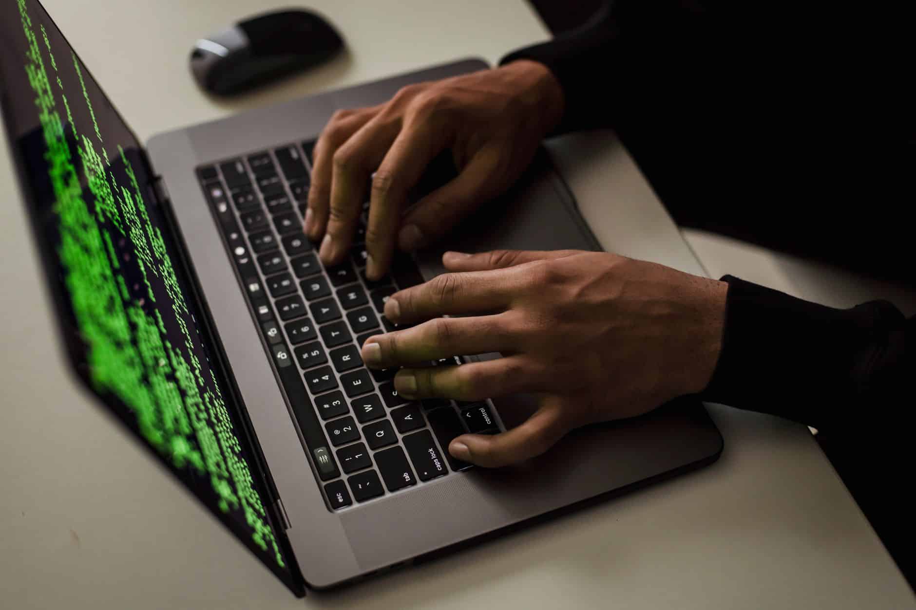 Mani su una tastiera di laptop con codice verde sullo schermo, simbolo di un attacco informatico. Binance