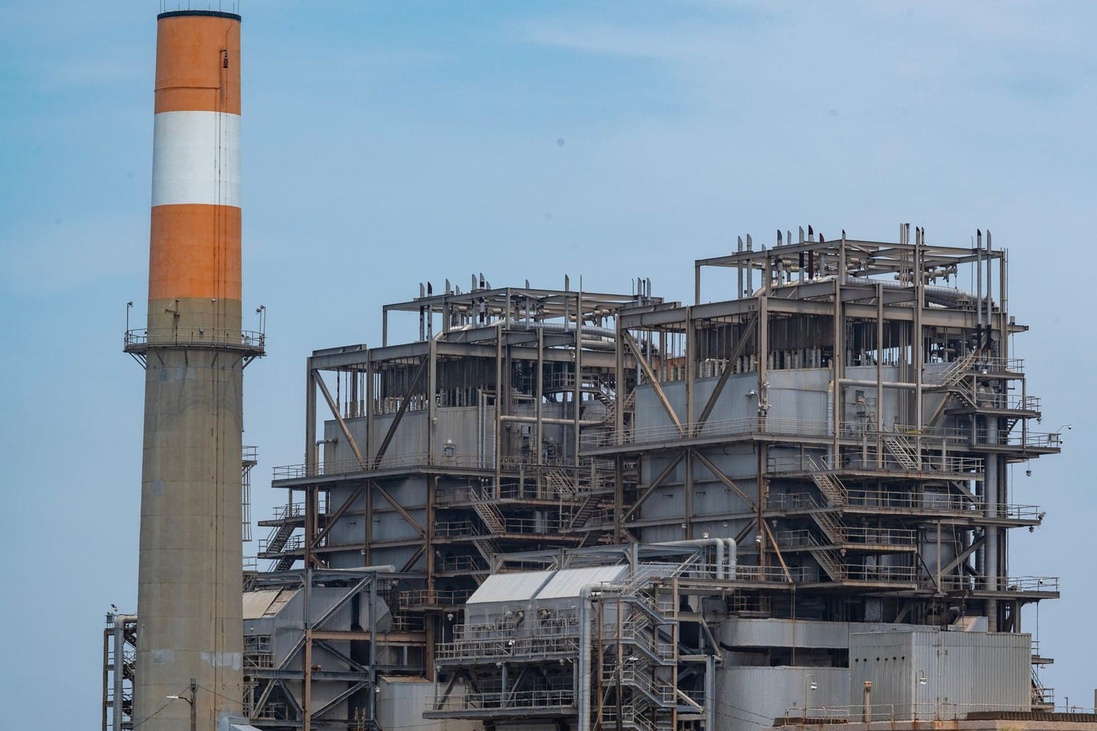 Centrale termoelettrica con ciminiera a strisce arancioni e bianche dietro le dune, immagine d'archivio per il confronto tra accumulo a batteria e centrali di punta