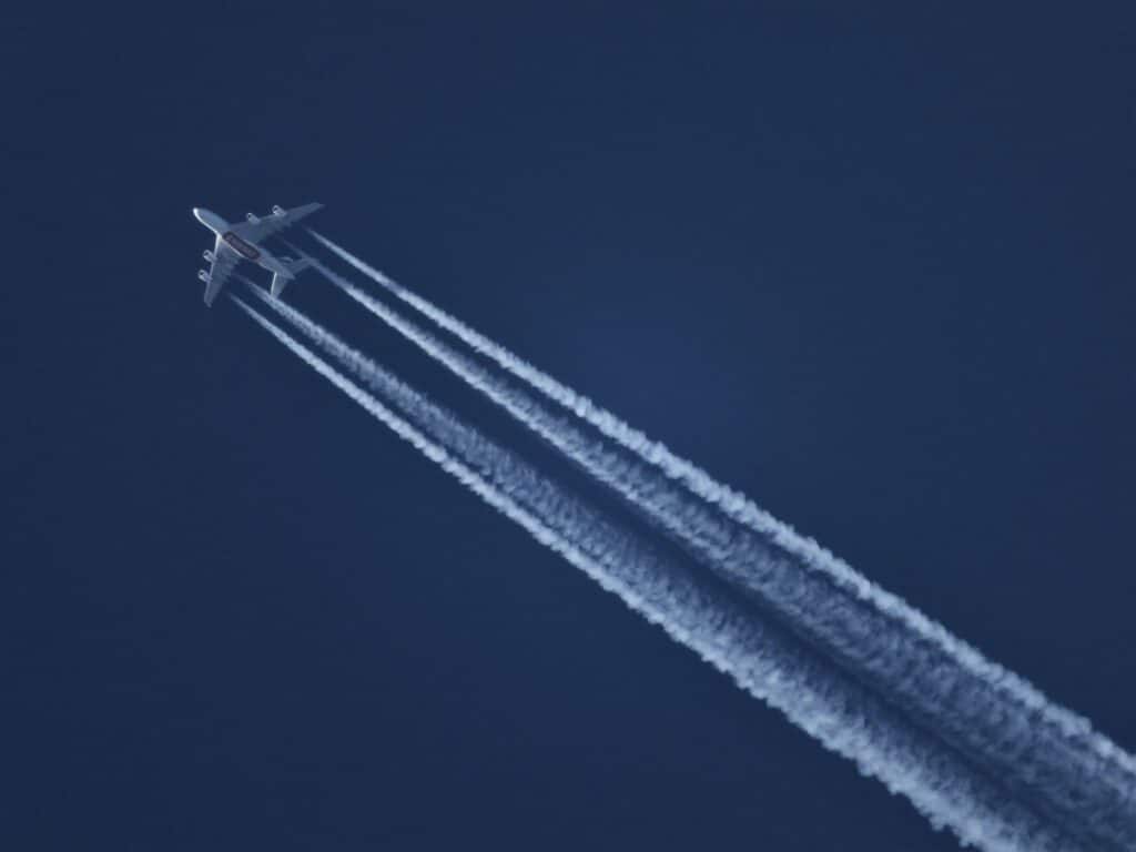 Un grande aereo a quattro motori in quota lascia quattro lunghe scie bianche in un cielo blu scuro. Contrails