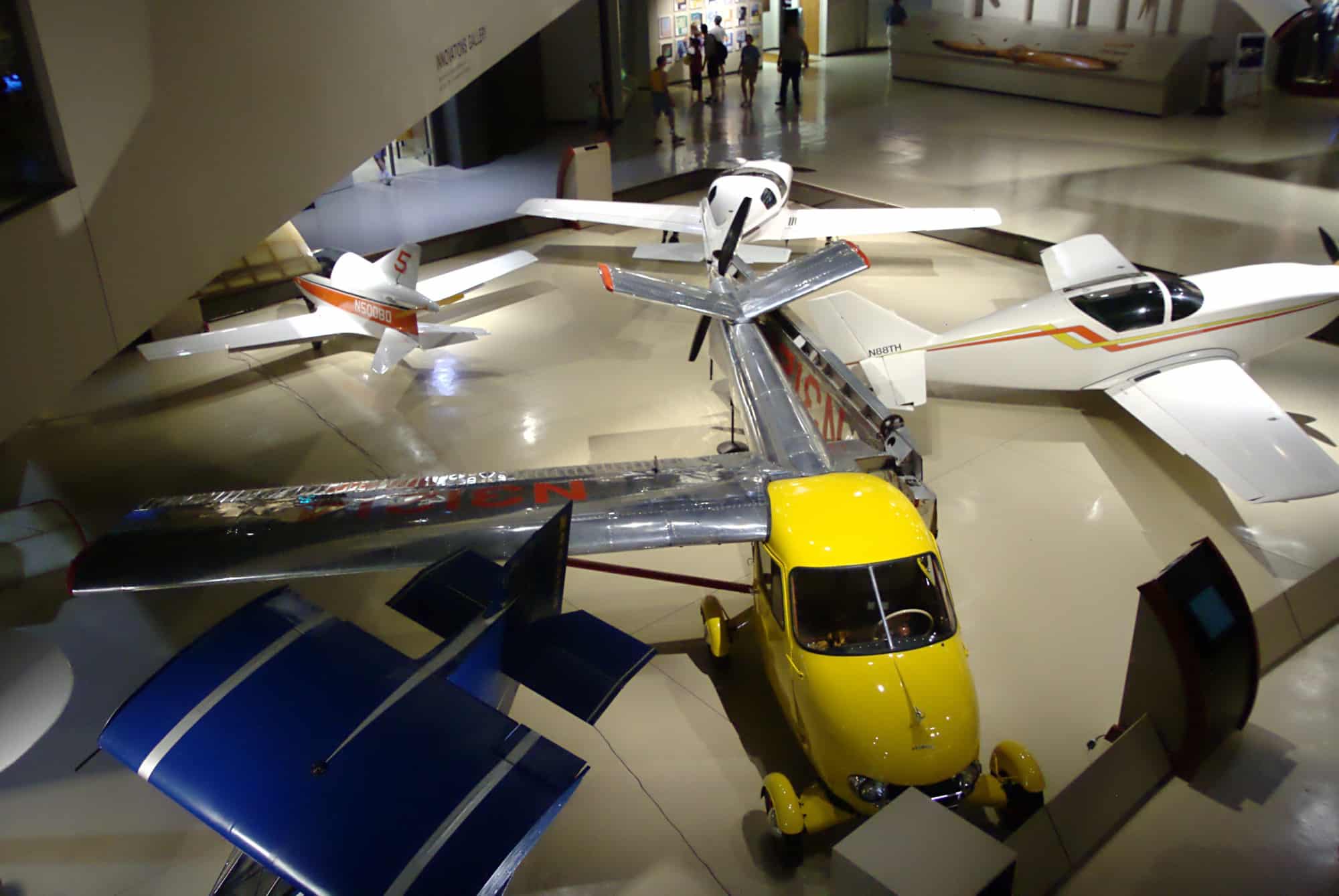 Aerocar giallo con l'ala smontata, esposto accanto ad altri aerei leggeri
