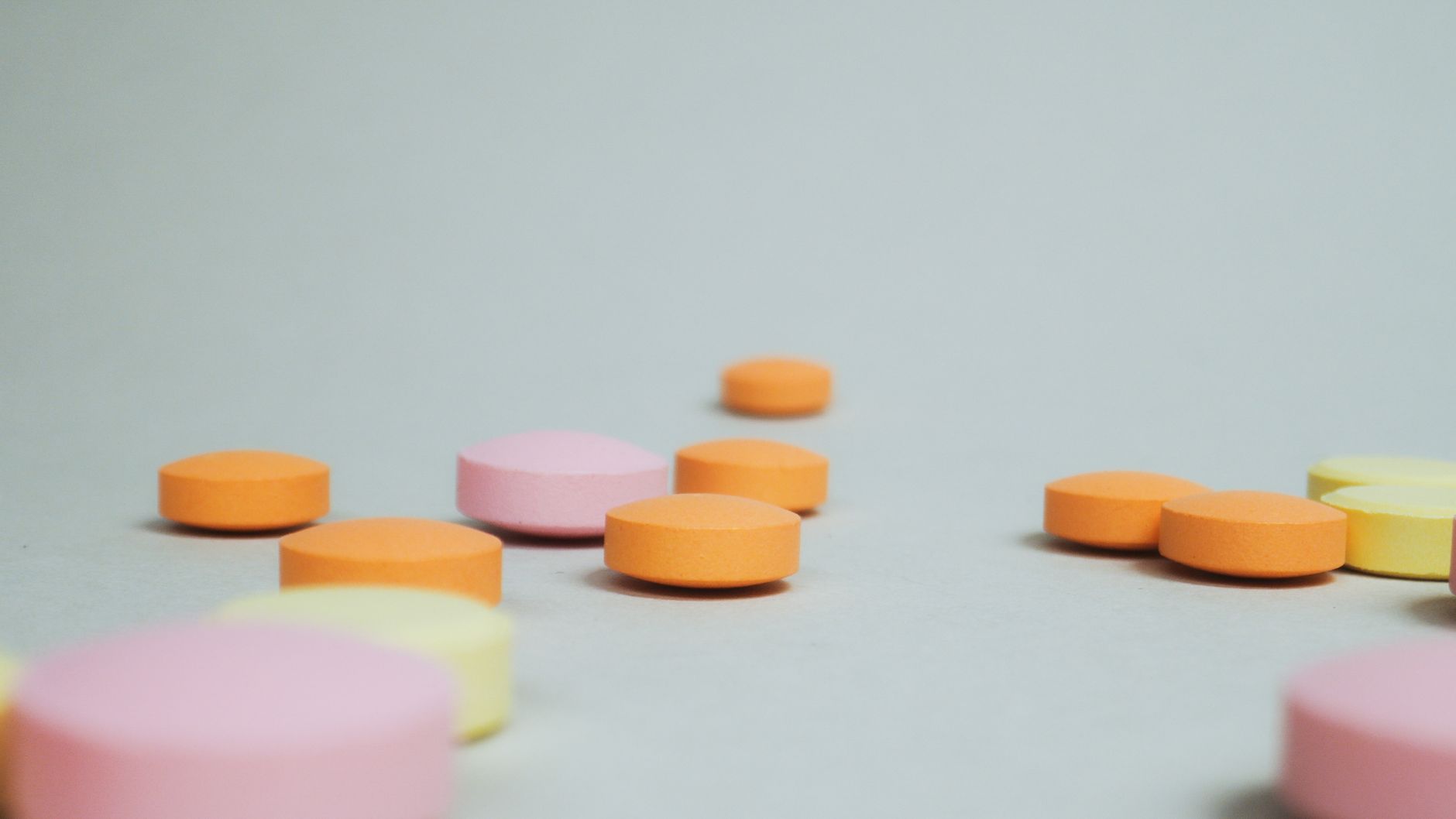Compresse tonde arancioni, rosa e gialle su un piano grigio, riprese a livello del tavolo. Minoxidil