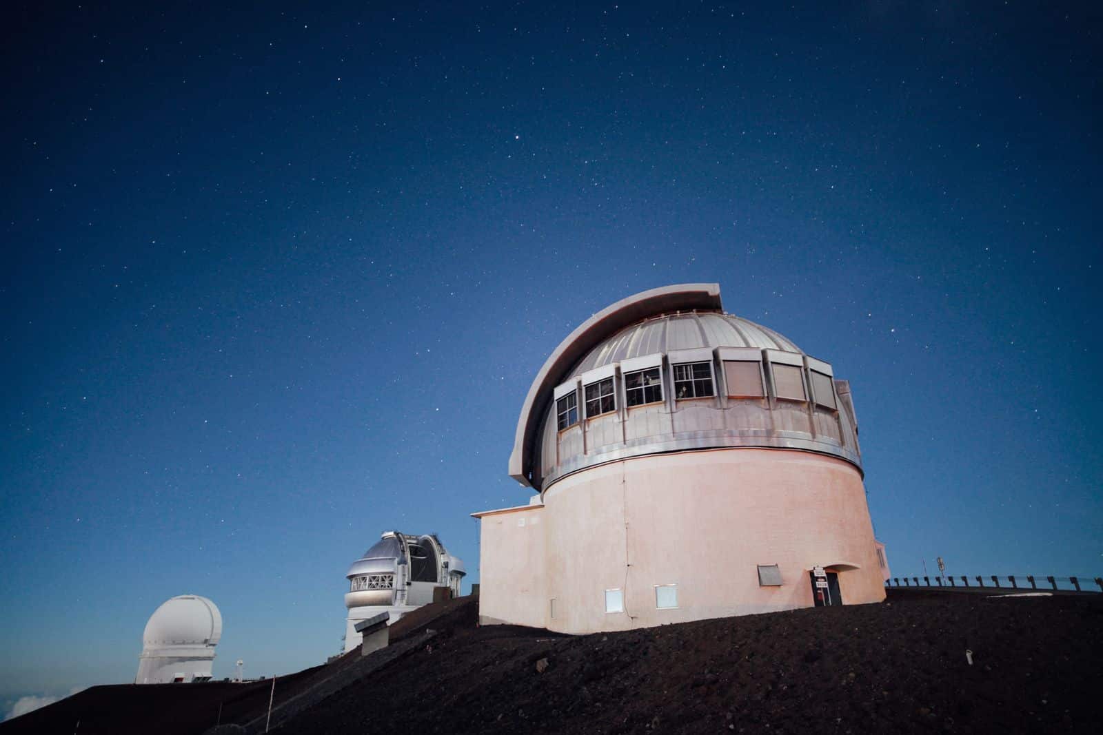 Una cupola di osservatorio astronomico sotto un cielo stellato, con altre due cupole sullo sfondo. Pianeta nano