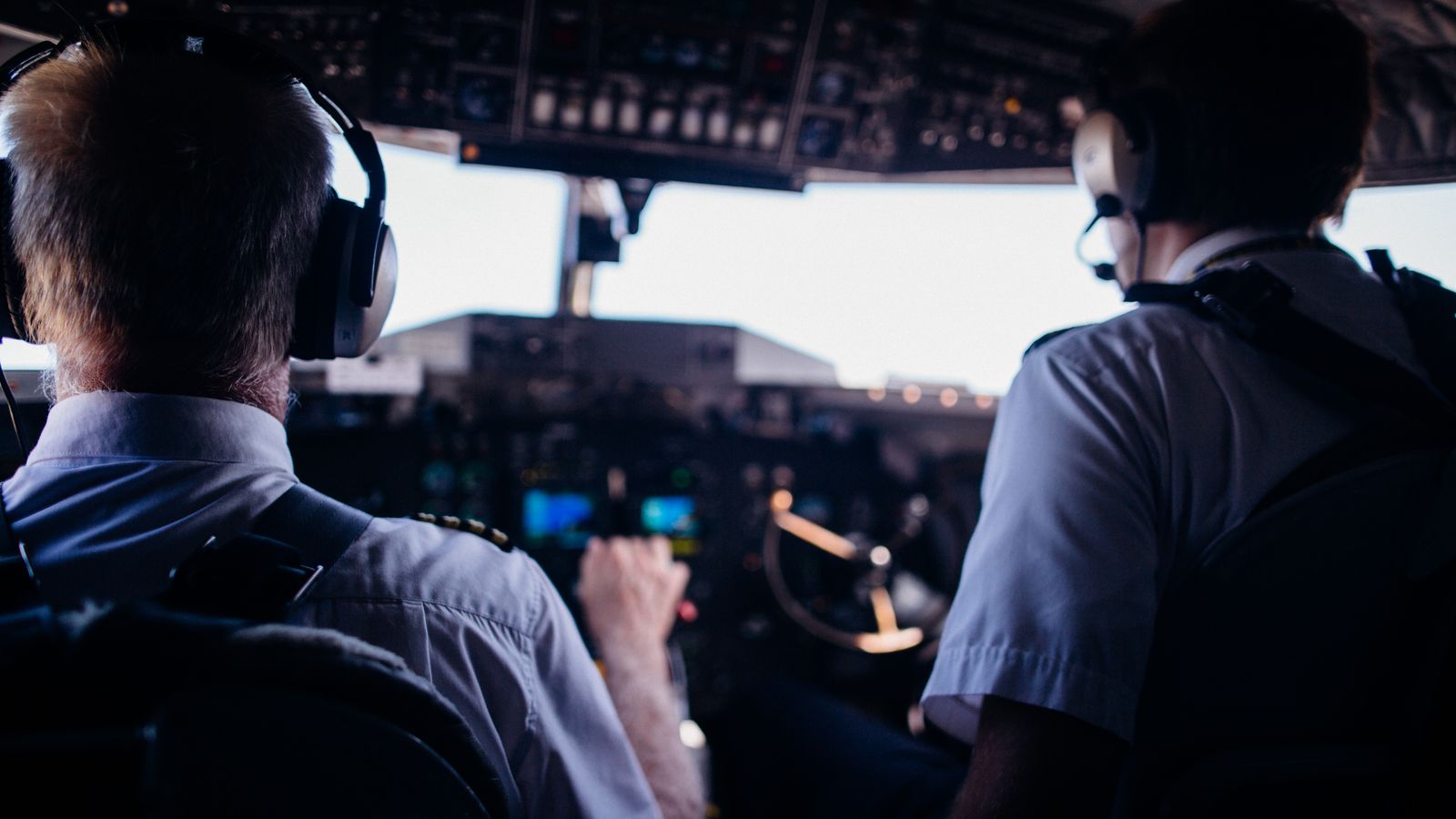 Due piloti in uniforme con le cuffie, visti di spalle, nella cabina di un aereo. Perdita di competenze