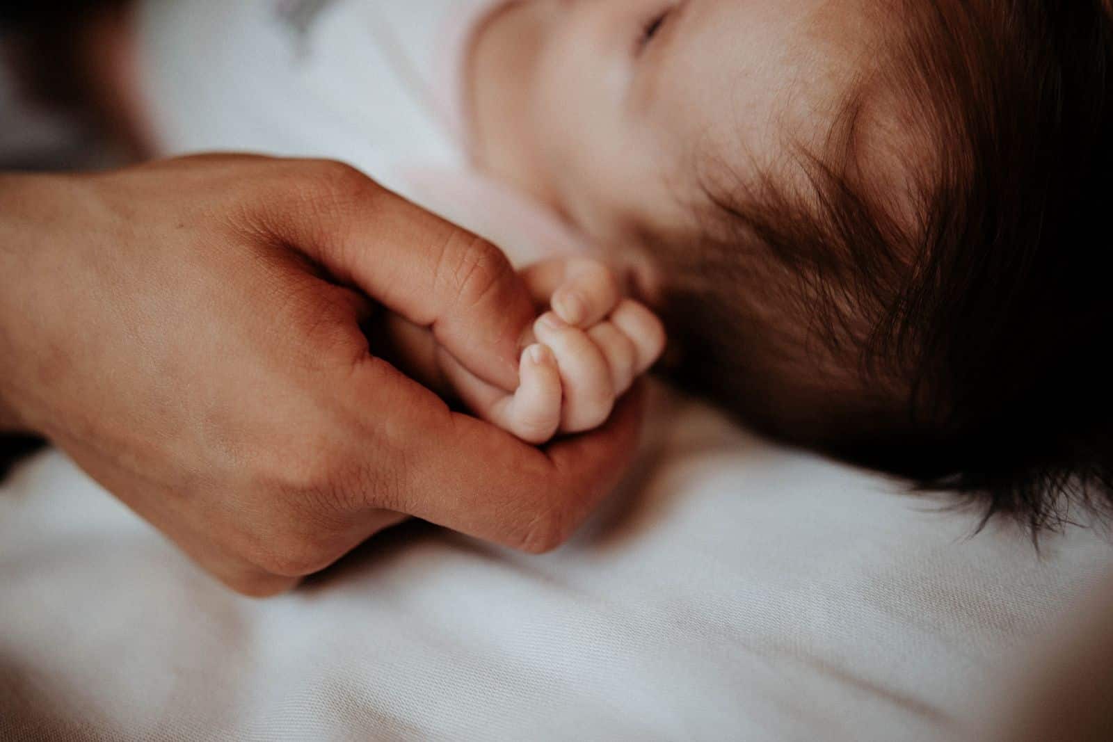 Mano di un adulto che stringe quella di un neonato addormentato, immagine della nascita nei casi di reincarnazione