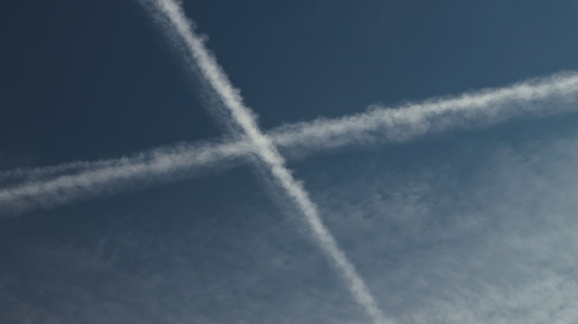Due scie di condensazione si incrociano a forma di X in un cielo azzurro scuro. Contrails